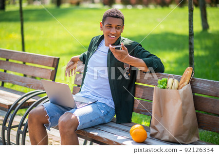 Guy saying message on smartphone sitting on bench Guy saying message on smartphone sitting on bench 92126334
