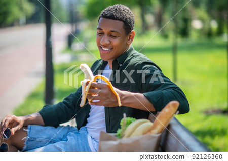 Guy looking at banana sitting on bench 92126360