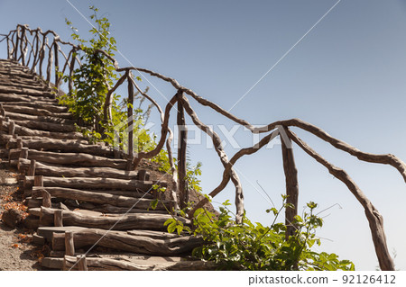 Wooden stairway with railings goes up the rocky coast 92126412