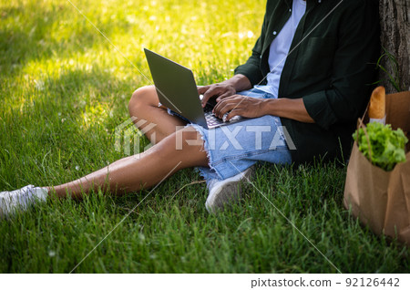 Hands of man sitting on grass typing on laptop 92126442