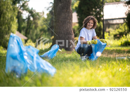 Kid in white tshirt gathering plastic litter in the park Kid in white tshirt gathering plastic litter in the park 92126550
