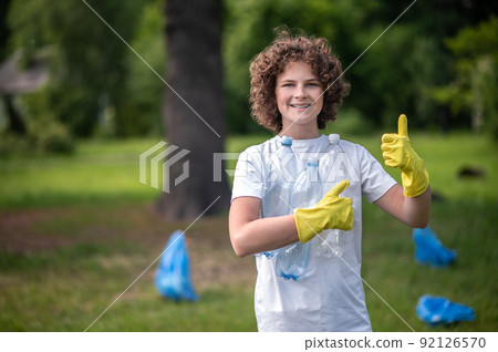Kid in yellow gloves in the park gathering garbage Kid in yellow gloves in the park gathering garbage 92126570