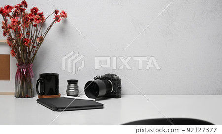 Freelancer workplace with camera, notebook, picture frame and flower pot on white table 92127377