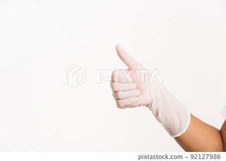 Woman wearing hand to blue rubber medical glove with thumb up finger 92127986
