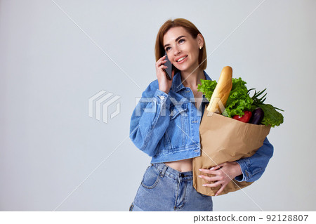 woman holding paper bag with vegetables and smartphone 92128807