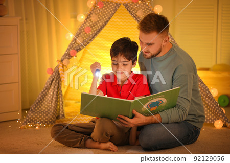 Father and son with flashlight reading book at home Father and son with flashlight reading book at home 92129056