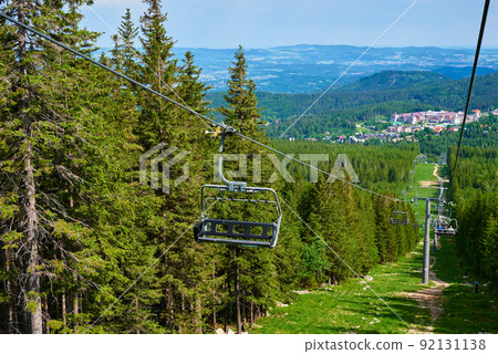 Open cable car line. Karpacz resort in Poland with lift road. Chairlift against green forest trees. Family outdoor recreation in mountains Open cable car line. Karpacz resort in Poland with lift road. Chairlift against green forest trees. Family outdoor recreation in mountains 92131138