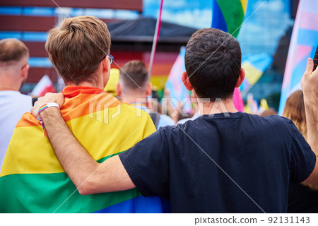 Two male friends standing under rainbow LGBTQ on pride parade. Tolerance, diversity and gender identity concept 92131143
