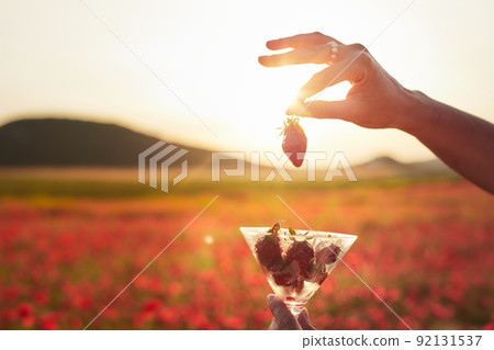 Strawberries in a glass against a field of poppies in the setting sun. Front view. Strawberries in a glass against a field of poppies in the setting sun. Front view. 92131537