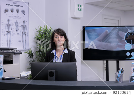 Portrait of smiling front desk receptionist waiting to greet patients in private practice clinic lobby. Professional healthcare worker offering support for hospital appointments. 92133654