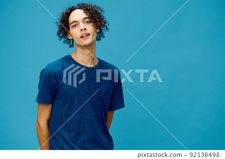 Smiling joyful cute curly tanned Caucasian guy in basic t-shirt posing isolated on over blue background. Lifestyle and Emotions concept. Good offer with copy space for ad Smiling joyful cute curly tanned Caucasian guy in basic t-shirt posing isolated on over blue background. Lifestyle and Emotions concept. Good offer with copy space for ad 92136498