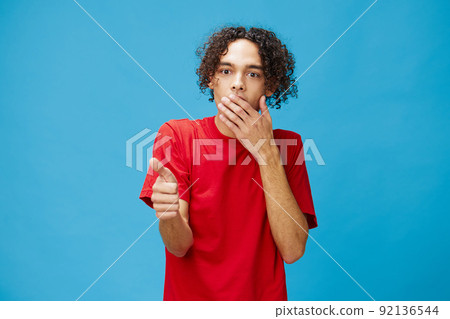 Excited shocked funny curly tanned Caucasian guy in basic red t-shirt show thumb up gesture Like posing isolated on blue background. Lifestyle and Emotions concept. Good offer with copy space for ad 92136544
