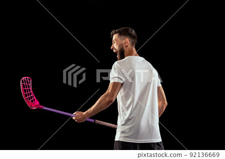 Studio shot of young man wearing sports uniform and sneakers playing floorball isolated on dark background. Sport, action and motion, movement, competition Studio shot of young man wearing sports uniform and sneakers playing floorball isolated on dark background. Sport, action and motion, movement, competition 92136669