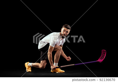 Studio shot of young man wearing sports uniform and sneakers playing floorball isolated on dark background. Sport, action and motion, movement, competition Studio shot of young man wearing sports uniform and sneakers playing floorball isolated on dark background. Sport, action and motion, movement, competition 92136670