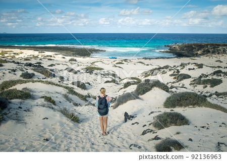 Female tourist visiting white beach of Caleta del Mojon Blanco. Sandy desert beach and rugged coastline. Orzola, Lanzarote, Canary Islands, Spain, Africa. Female tourist visiting white beach of Caleta del Mojon Blanco. Sandy desert beach and rugged coastline. Orzola, Lanzarote, Canary Islands, Spain, Africa. 92136963