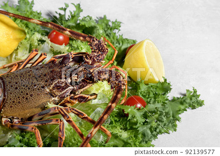 Fresh spiny lobster or sea crayfish with salad, tomatoes and lemon, preparation for cooking common Mediterranean lobster Fresh spiny lobster or sea crayfish with salad, tomatoes and lemon, preparation for cooking common Mediterranean lobster 92139577