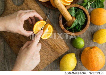 Top table view of female hands cutting orange, citrus fruits around 92139938