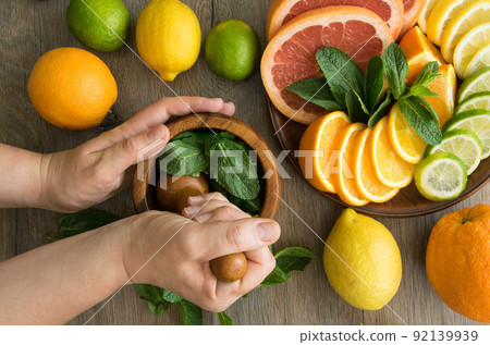 Top view hands pounding mint with pestle in mortar, citrus on dish Top view hands pounding mint with pestle in mortar, citrus on dish 92139939