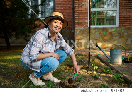 Beautiful Caucasian woman, farmer agronomist using garden shovel, digging soil and making a hole for planting seedlings,  92140233