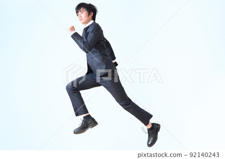 A business person in a suit who jumps while holding a smartphone in his hand 92140243