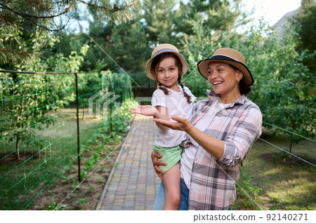 Instilling love for farming from childhood. Mom and daughter, hold copy space on hands palms up, in family organic farm  92140271