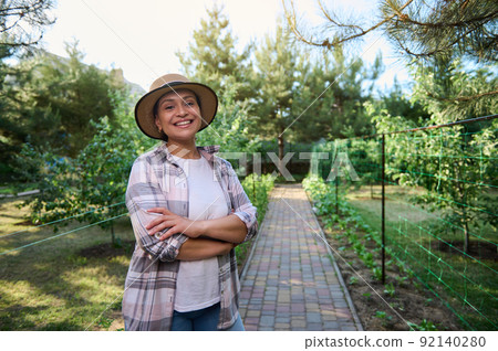 Pleasant Caucasian woman, farmer smiling toothy smile, standing by row of seedlings in the organic vegetable garden Pleasant Caucasian woman, farmer smiling toothy smile, standing by row of seedlings in the organic vegetable garden 92140280
