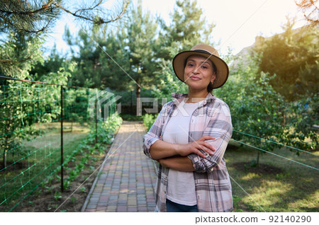 Pleasant female farmer looking at camera while standing at organic farm that growing eco-friendly fruits and vegetables  92140290