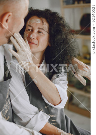 Mutual creative work. Adult elegant couple in casual clothes and aprons. People creating a bowl on a pottery wheel in a clay studio. Mutual creative work. Adult elegant couple in casual clothes and aprons. People creating a bowl on a pottery wheel in a clay studio. 92140525