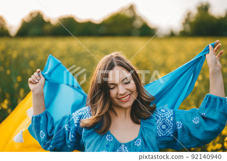 Happy ukrainian woman with national flag on canola blossom meadow background. Portrait of young girl 92140940