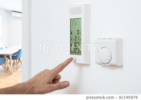 Hand activates burglar alarm control panel on wall in home office workplace interior 92140979