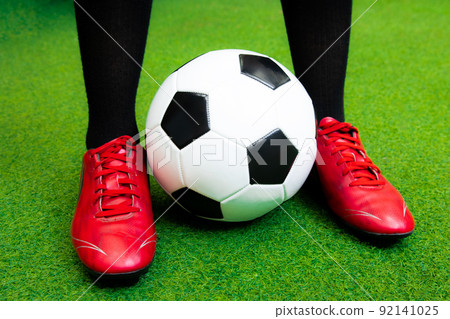 Close up football player with red soccer shoes and black and white ball on artificial grass.	 92141025