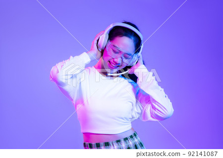 Young asian woman in white shirt wearing headphones posing on blue and purple background.. 92141087