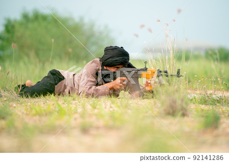 Terrorist with veil lie on the ground and point gun to the enemy in grass field with day light. Terrorist with veil lie on the ground and point gun to the enemy in grass field with day light. 92141286