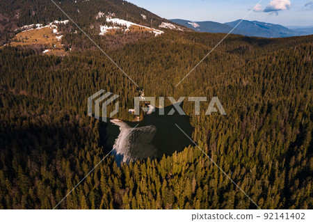 Lake Synevyr framed by a pine forest in the Carpathians, drone view, Synevyr Glade National Nature Park. Lake Synevyr framed by a pine forest in the Carpathians, drone view, Synevyr Glade National Nature Park. 92141402