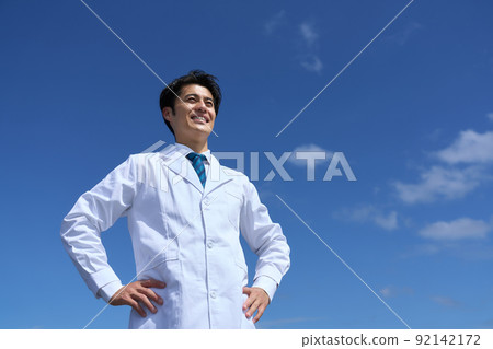 一個身穿白大褂的男人在藍天下雙手叉腰微笑著向前看 92142172