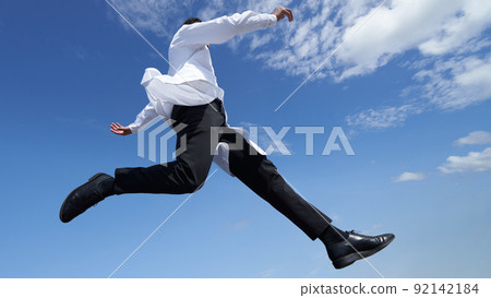 A man in a white coat jumping under the blue sky 92142184