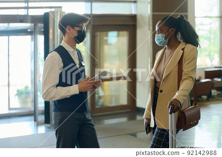 Young male receptionist in uniform and mask consulting black woman 92142988