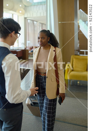 Young black woman with suitcase looking at bellboy or receptionist meeting her 92143022