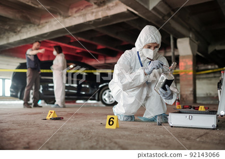 Young criminological expert in coveralls inspecting empty bottle on crime scene Young criminological expert in coveralls inspecting empty bottle on crime scene 92143066