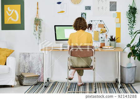 Rear view of young female freelancer in casualwear sitting by workplace Rear view of young female freelancer in casualwear sitting by workplace 92143288
