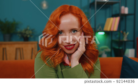 Close-up of happy beautiful teenager redhead ginger woman smiling looking at camera at home on couch Close-up of happy beautiful teenager redhead ginger woman smiling looking at camera at home on couch 92144836