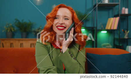 Red hair woman enjoying smartphone call talking, mobile phone conversation with friends at home Red hair woman enjoying smartphone call talking, mobile phone conversation with friends at home 92144840