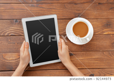Girl hands with digital tablet and cup of coffee on a wooden table Girl hands with digital tablet and cup of coffee on a wooden table 92144973