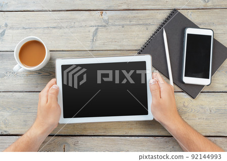 hands of a man holding blank tablet device over a wooden workspace table hands of a man holding blank tablet device over a wooden workspace table 92144993