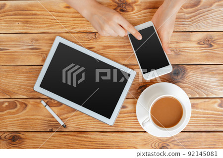 Girl hands with digital tablet and cup of coffee on a wooden table Girl hands with digital tablet and cup of coffee on a wooden table 92145081