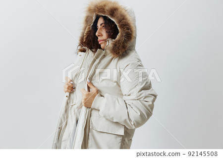Serious Curly Pretty Latin Lady Wearing Fur Hood Of Soft Warm Beige Winter Coat Posing Isolated Looking Aside At White Studio Background. Fashion Huge Sale New Collection Concept Vertical Side Shot 92145508
