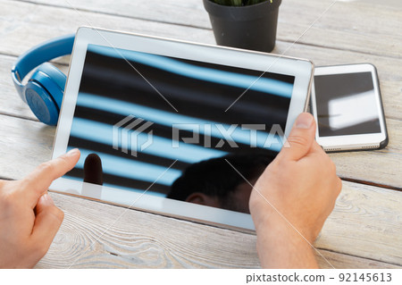 hands of a man holding tablet device over a wooden workspace table hands of a man holding tablet device over a wooden workspace table 92145613