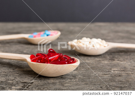 Vitamin capsules in a spoon on a colored background. Pills served as a healthy meal. Red soft gel vitamin supplement capsules on spoon 92147037