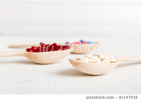 Vitamin capsules in a spoon on a colored background. Pills served as a healthy meal. Red soft gel vitamin supplement capsules on spoon 92147038
