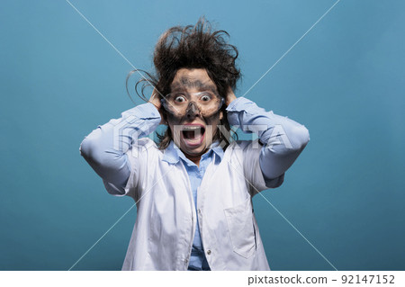 Psycho and scared mad chemist screaming in panic after dangerous chemical explosion and failed scientific experiment. Weirdo scientist with messy hair and dirty face shouting on blue background. Psycho and scared mad chemist screaming in panic after dangerous chemical explosion and failed scientific experiment. Weirdo scientist with messy hair and dirty face shouting on blue background. 92147152